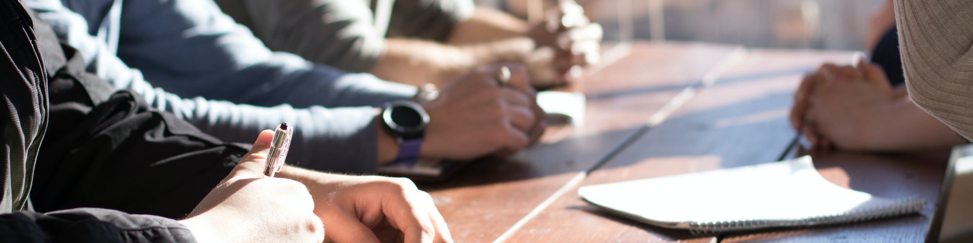 people sitting on chair in front of table while holding pens during daytime