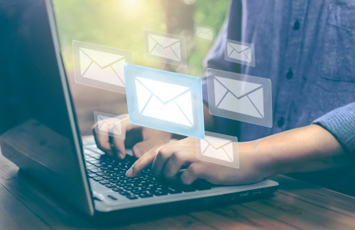 Person typing on a laptop with email illustrations popping up